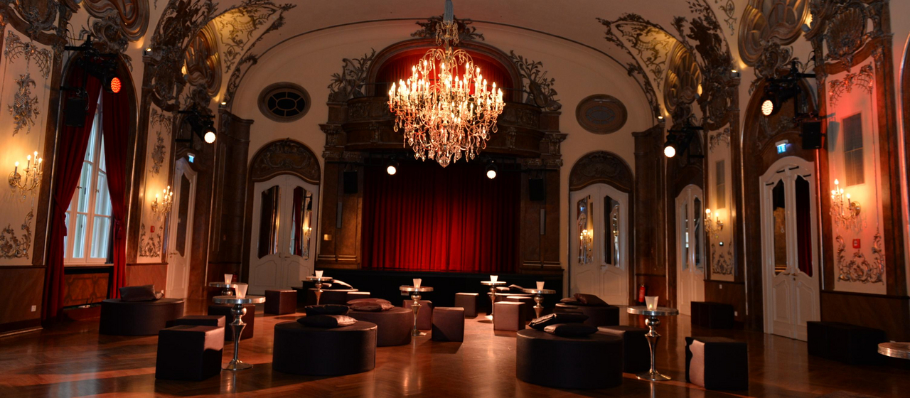 romantischer Theatersaal mit schwarzen Sesseln unter einem Kronleuchter in München