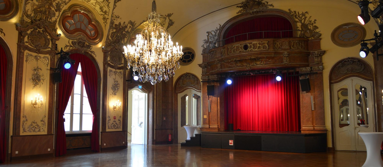 Foto des Silbersaals ohne BEstuhlung mit rotem Vorhang und Kronleuchter